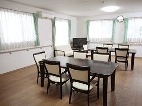 リビングには、２卓の木製テーブルセットがゆとりのある間隔で置かれていて、テレビもある。室内は広く落ち着いた雰囲気で、壁沿いには手すりがある。