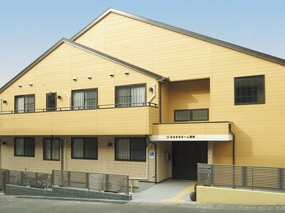 黄色の２階建ての建物は、アットホームな雰囲気である。外側に横格子のフェンスを設置している。玄関前に点字ブロックを備えている。