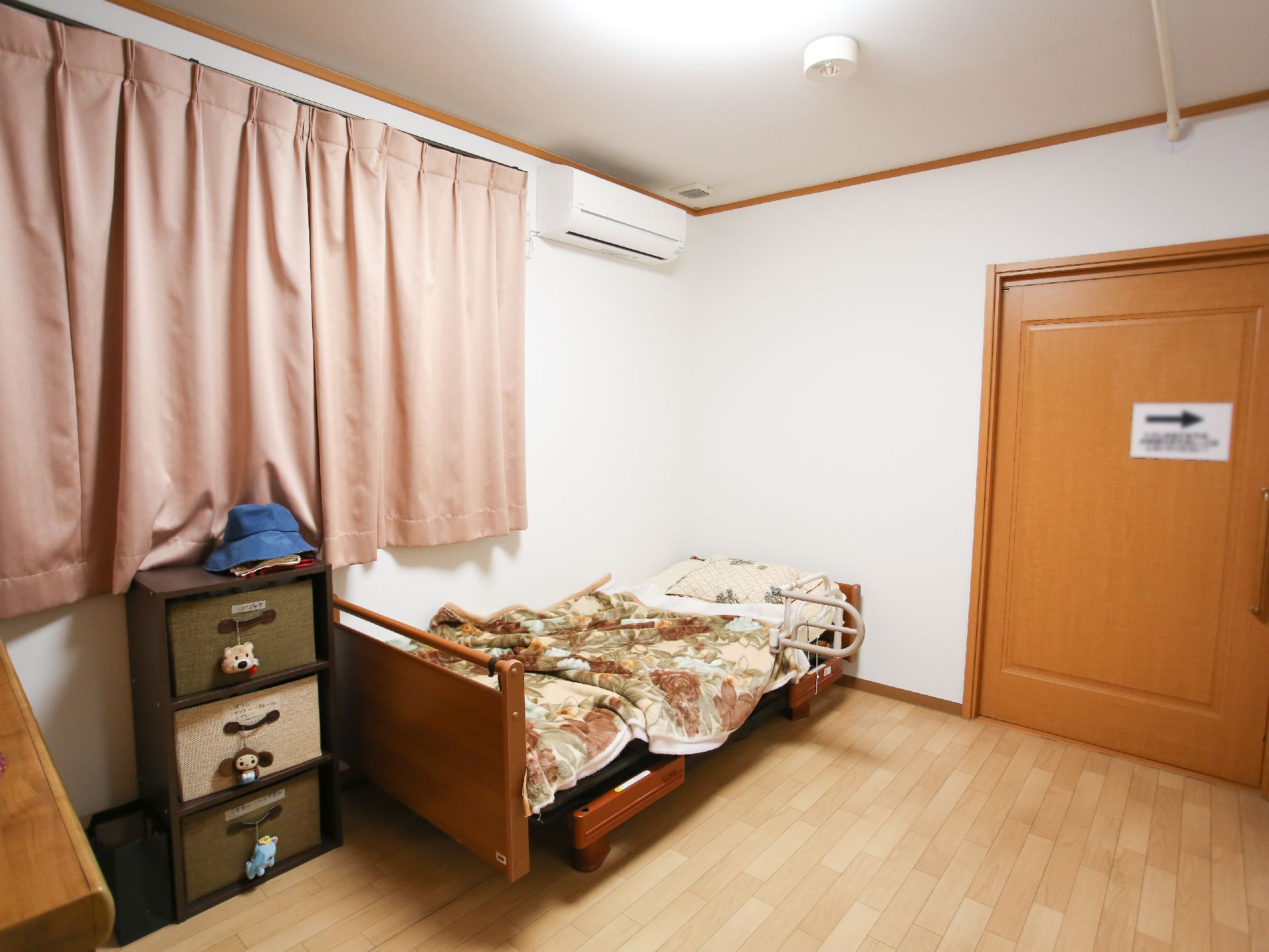 左にあるブラインドのかかった窓を背に、テーブルについて新聞を広げている高齢男性