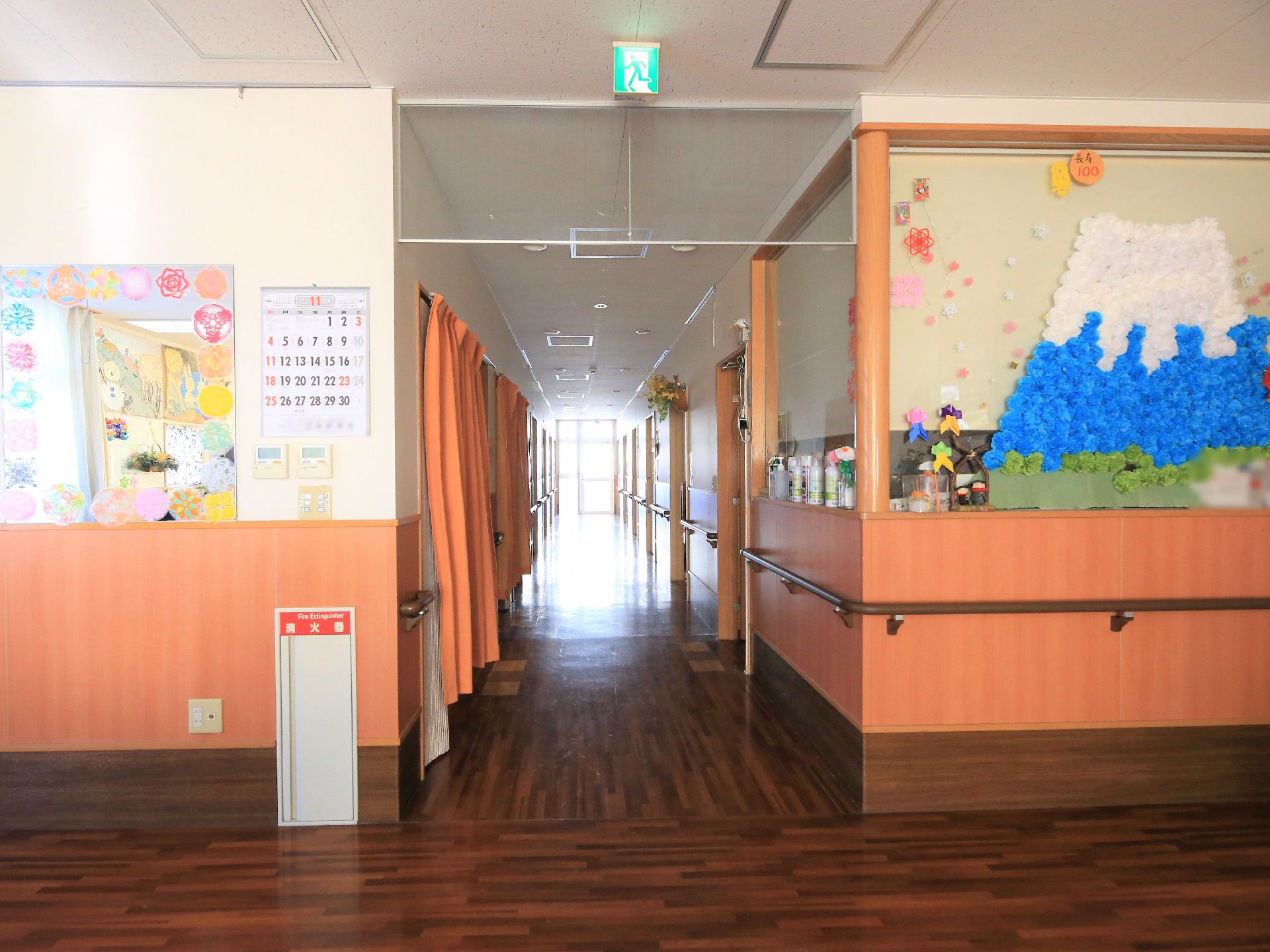 廊下の床面は濃い茶色になっている。廊下の角の大きなガラス窓には、紙で作られた３種類の色の花を組み合わせた山の風景の作品が展示されている。