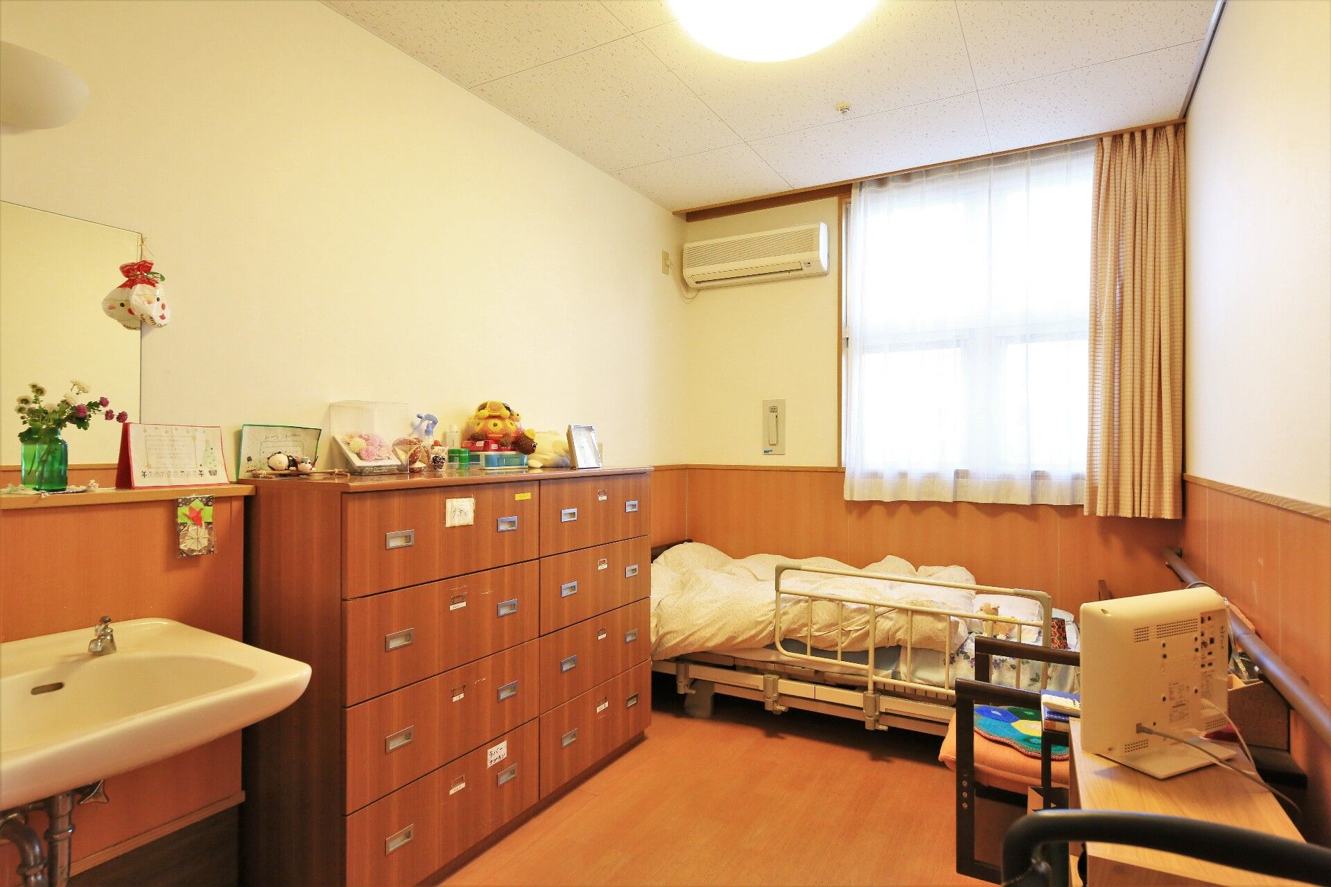 正面に窓がありその左の壁面上部にエアコン、窓の下にベッドがある居室