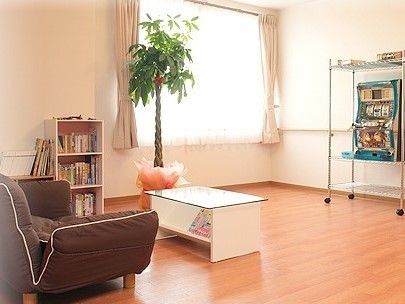 正面に窓、その前に観葉植物、さらに手前に白いテーブルと茶色のソファがあるスペース