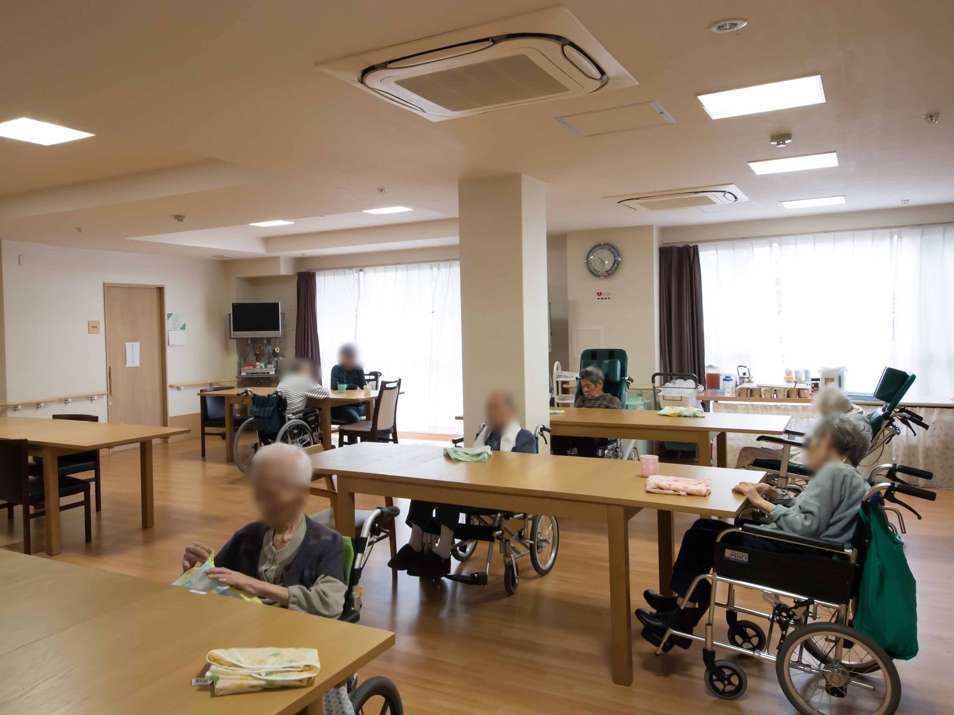 白と木目を基調とした共有スペースである。天井にエアコンと四角形の照明を間隔を置いて設置している。角にテレビを備えている。