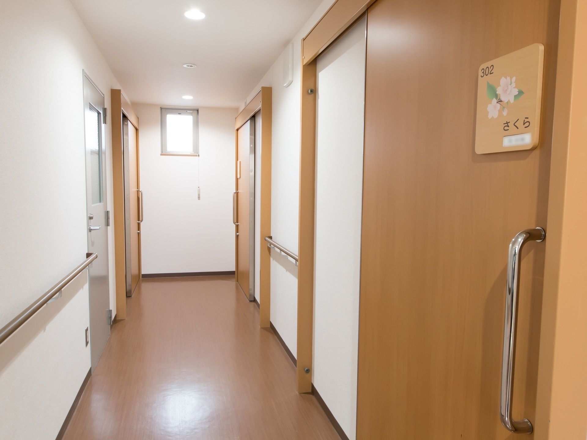 居室が並ぶあたたかい雰囲気あふれる廊下。各扉はスライド式となっており、部屋番号と花の絵が描かれた表札が設置されている。