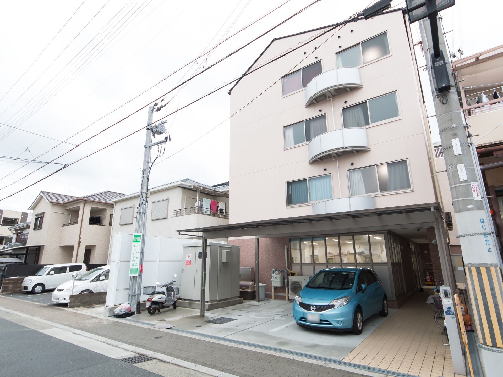 ４階建ての白を基調としたグループホームである。敷地内にはアスファルトで舗装された屋根付きの駐車場が設けられている。