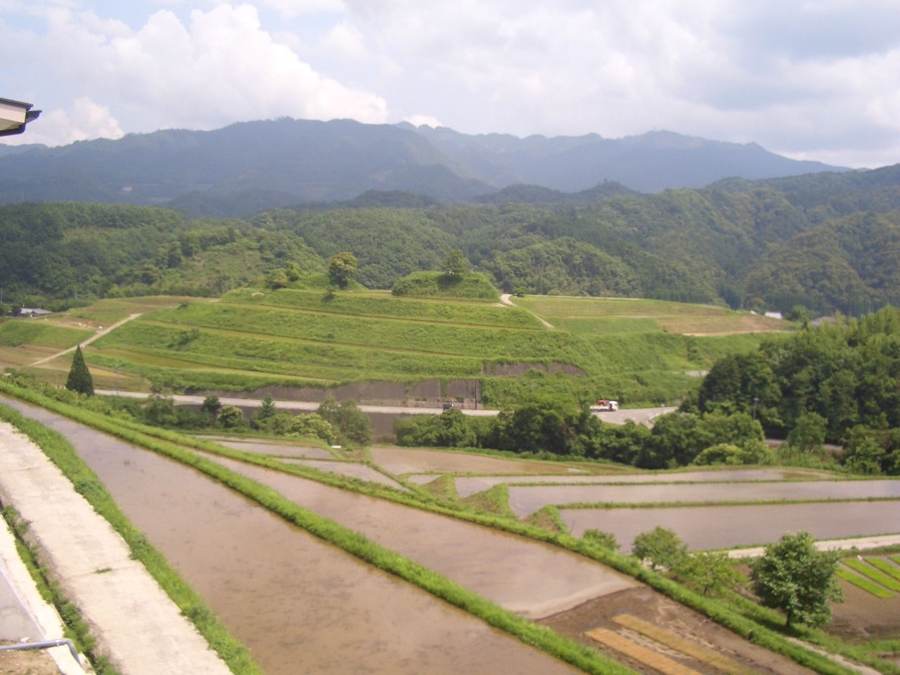 遠景に山並みが見え、その手前に段々になった農地、一番手前に棚田が見える景観