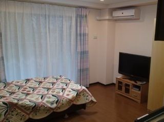 左正面にレースのかかった窓、その手前にベッド、右の壁面にテレビがある居室