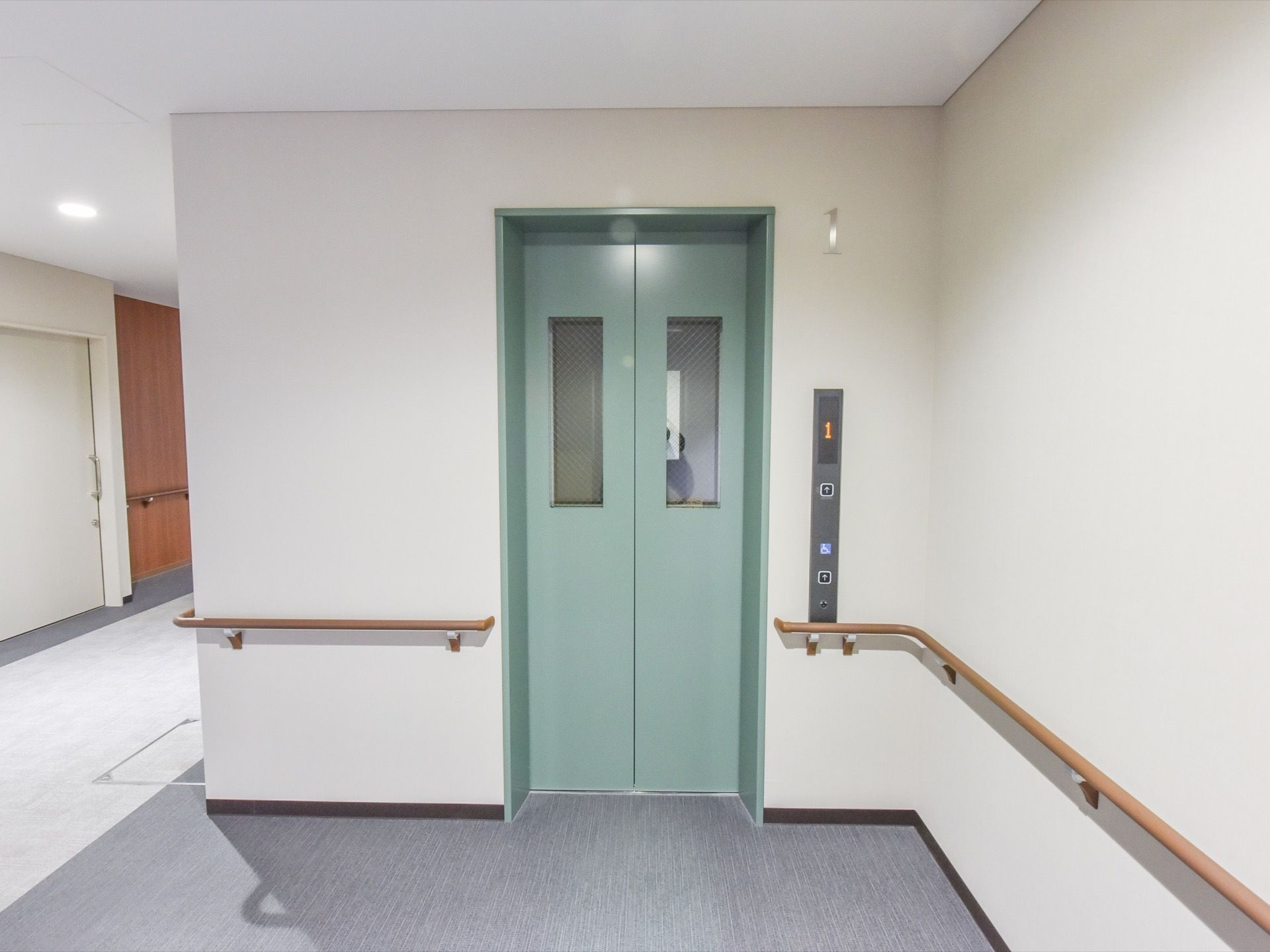 廊下とエレベーター前の床は濃い色と薄い色で分けられている。扉は薄い緑系の色で、窓にはガラスがはめ込まれている。