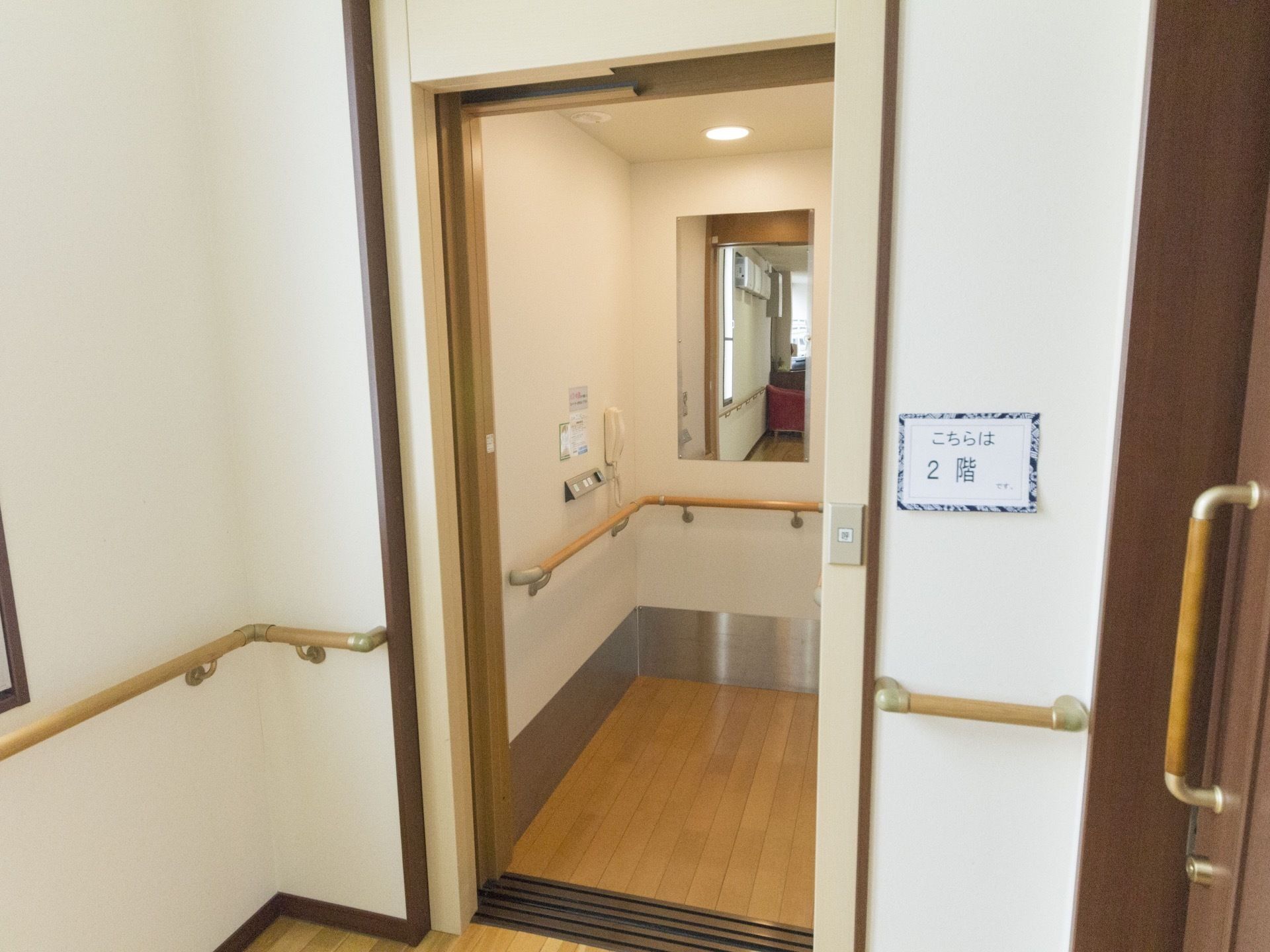 エレベーターの扉が開いている。手すりが外から中へ移動に不安がないように設置されている。庫内には各階への連絡がとれる電話も設置されている。