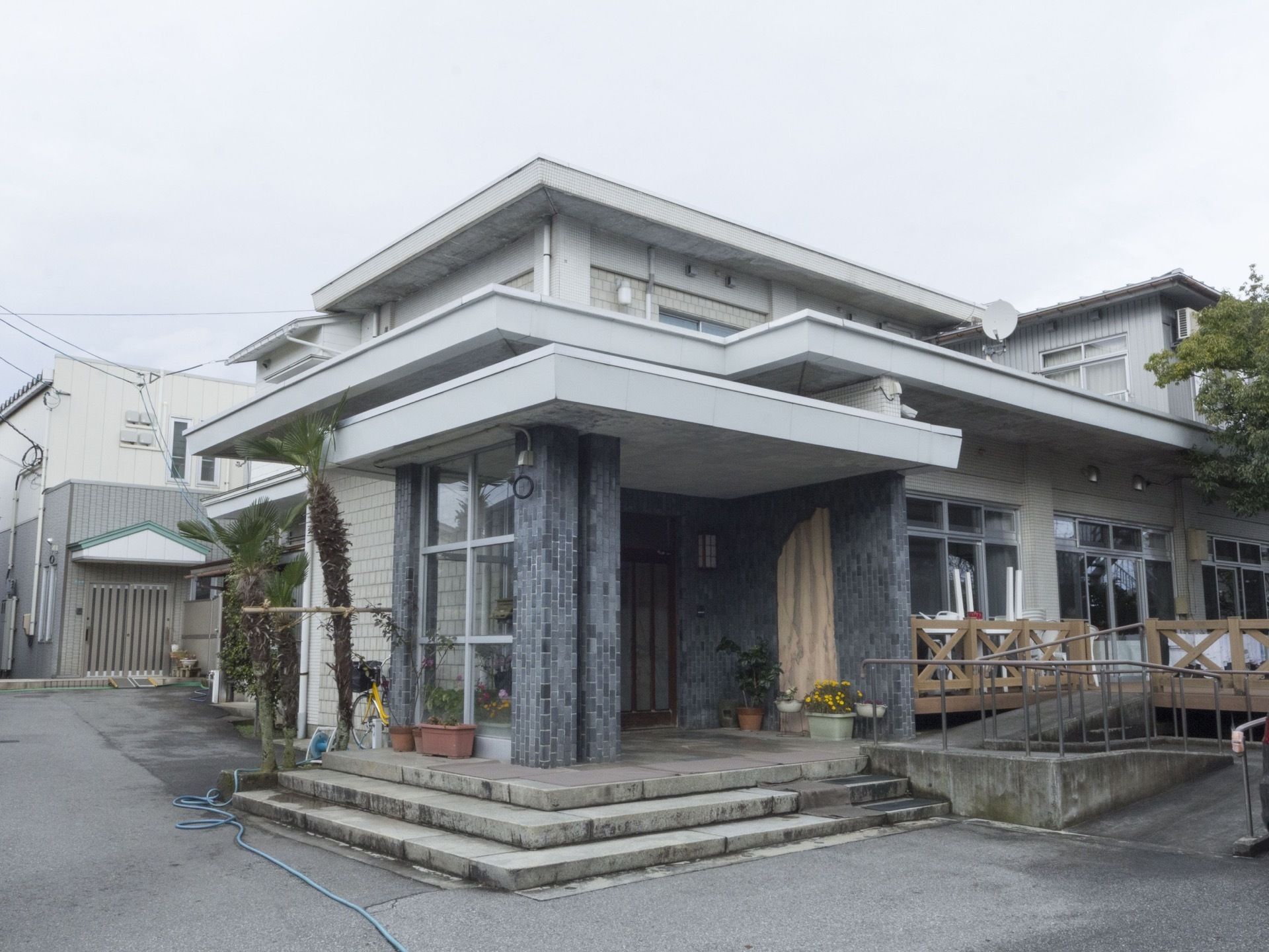 玄関周りのグレーのレンガが印象的な外観である。３段の低い階段になっているが、横には手すりの付いたスロープがある。