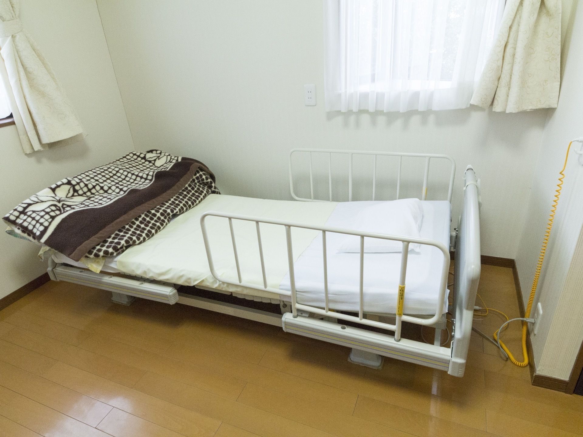 左と右に窓があり、その間の茶色の床にガード付きのベッドが置かれた居室