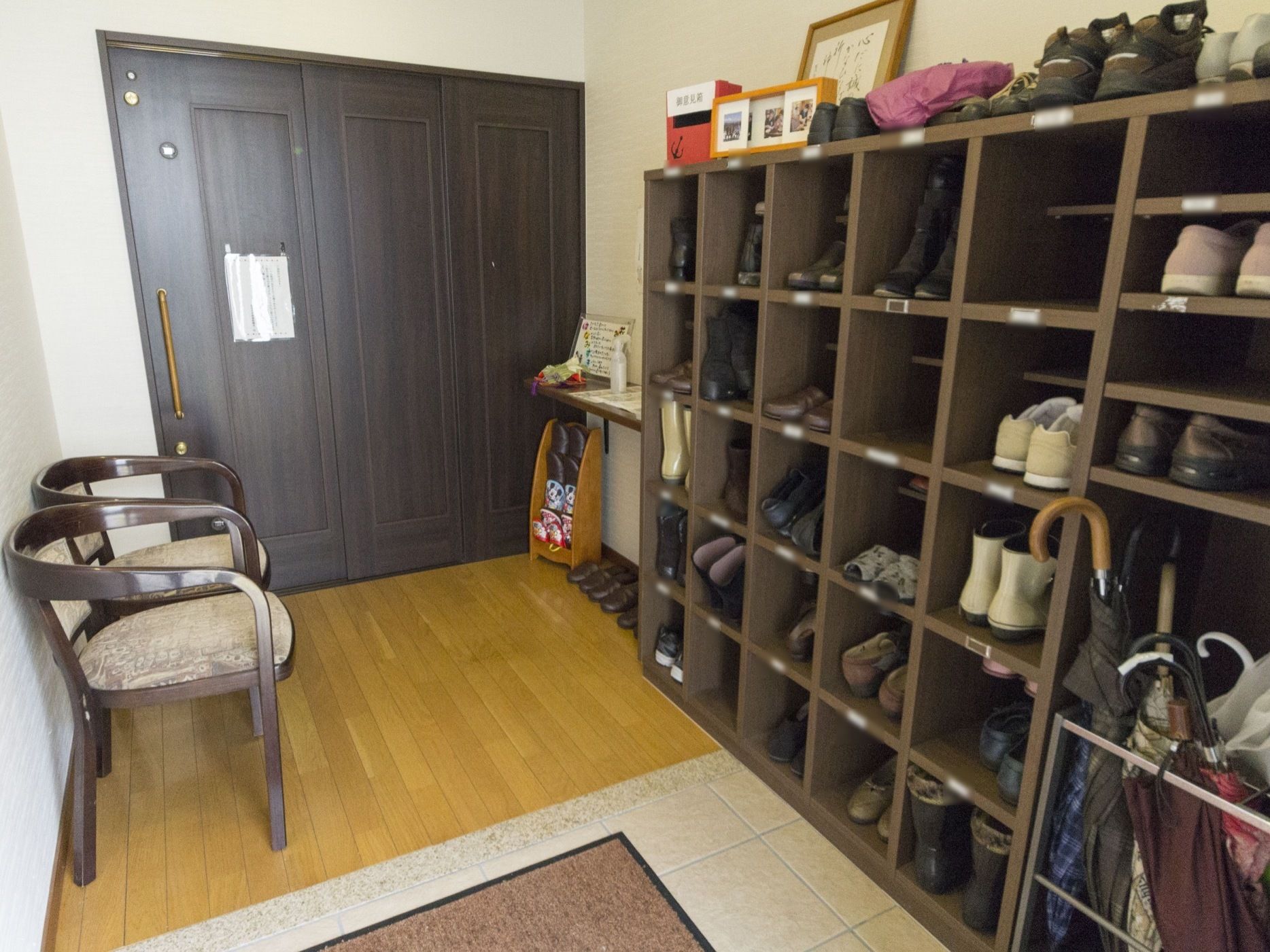 玄関に入居者様向けの靴箱と傘立てを設置し、履物を替えやすいように２脚の椅子を用意している。来訪者様のスリッパも完備している。