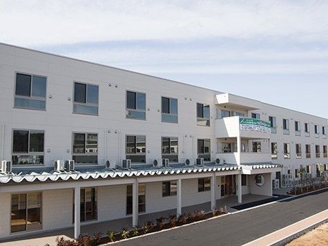左からひさしのかかる玄関前まで波板の屋根の通路が設けられた白い3階建ての建物