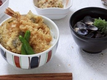 海老をはじめとする天ぷらがたっぷりと盛られた天丼。お椀の中には貝が山盛りに入った汁物があり、小鉢や香の物もついている。