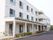 白い3階建の施設である。1階部分には庇が設置されいる。建物前には、ツツジなどの植物が植えられている花壇がある。
