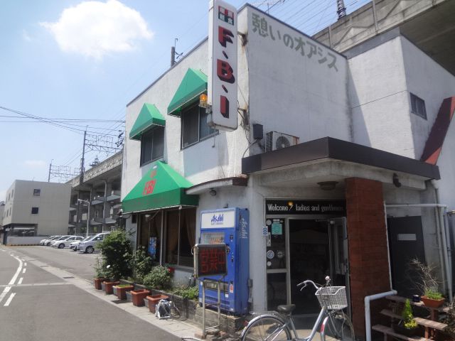 施設の北側にある喫茶店の前には植木が並べられている。線路下にたたずむ白い壁に、緑のテントがかわいらしい建物である。