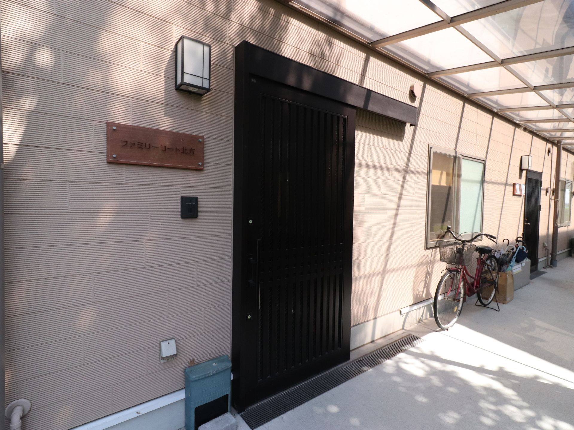 ポリカーボネート製の屋根が付いた通路には、施設内に入れる裏口がある。扉は引き戸になっており、壁に施設名が書かれたプレートが設置されている。