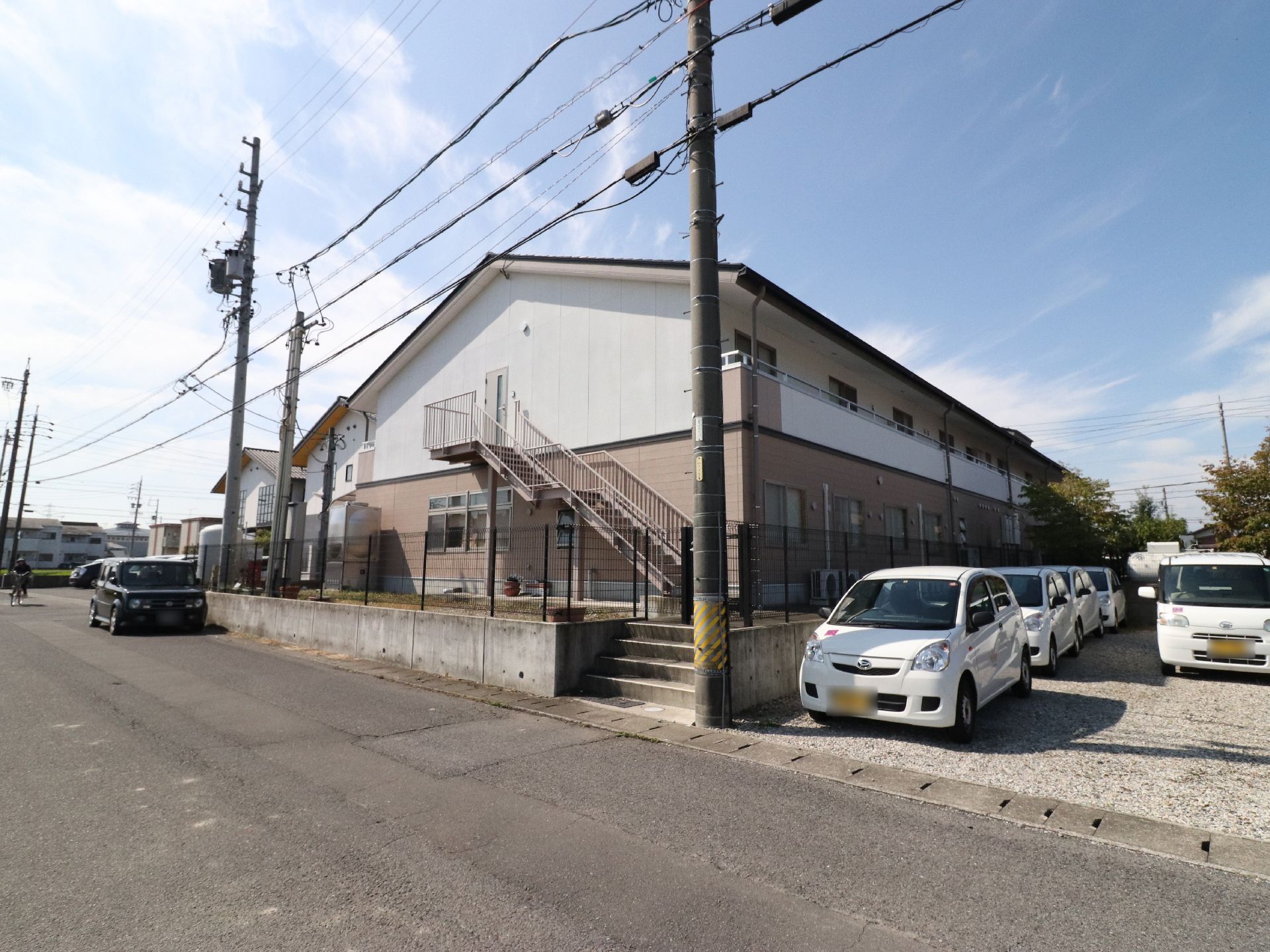 外壁が白と薄いピンク色をした建物である。2階の側面に外階段が付いている。敷地は、フェンスで囲まれている。
