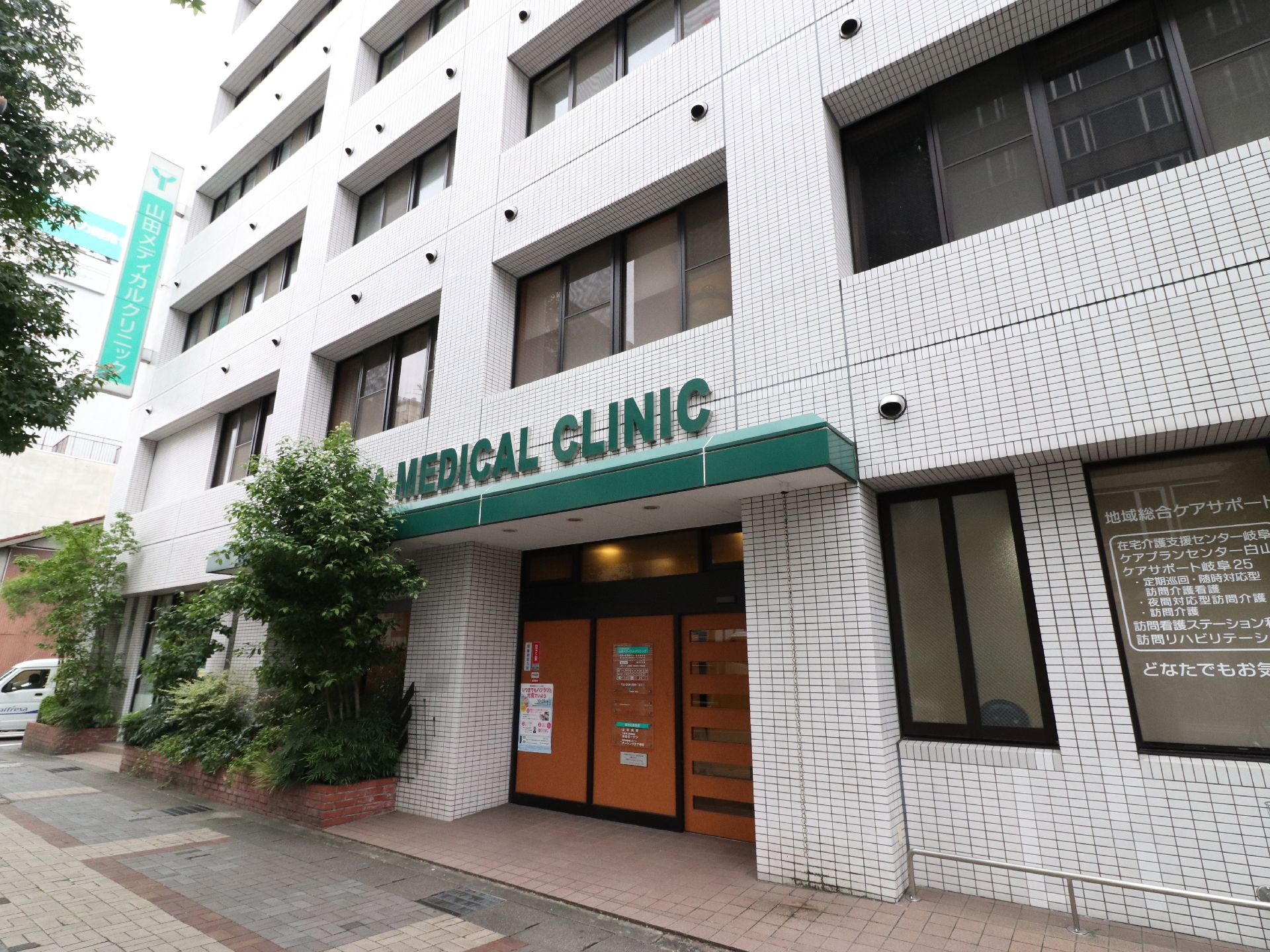 施設の協力医療機関として連携しているクリニックの玄関。黒い枠に木目調のドアである。グリーンのひさしの上にグリーンの文字で看板がかかっている。