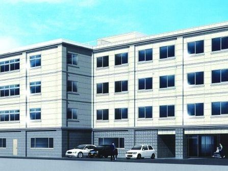 ４階建ての建物は白とグレーですっきりとした印象。玄関前には車いすの利用者を介助している人がいる。