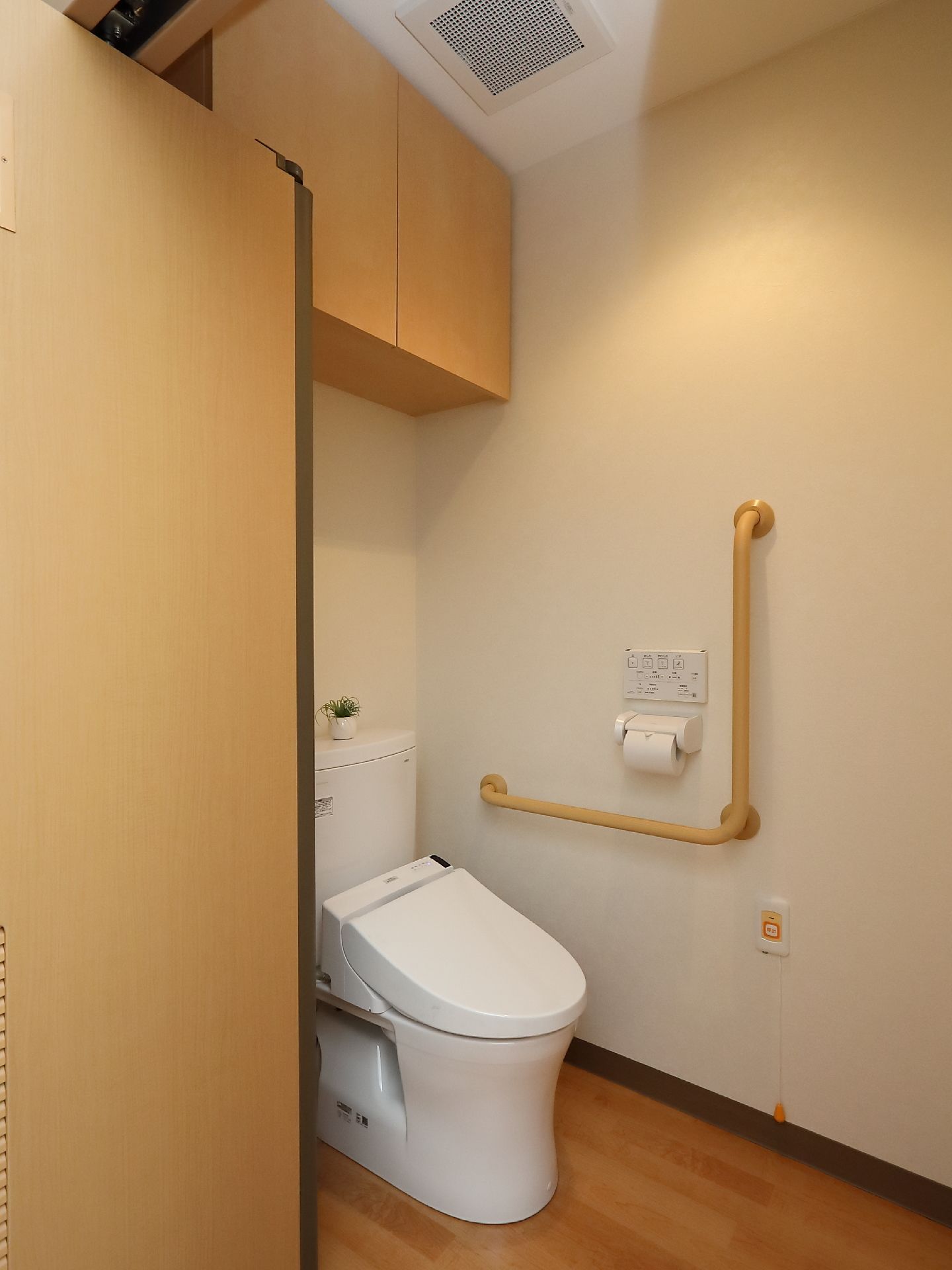 トイレの壁には手すりや緊急ボタンを取りつけて、安全に使用できる配慮がされている。収納の棚もあり、トイレ用品など入れておくことができる。