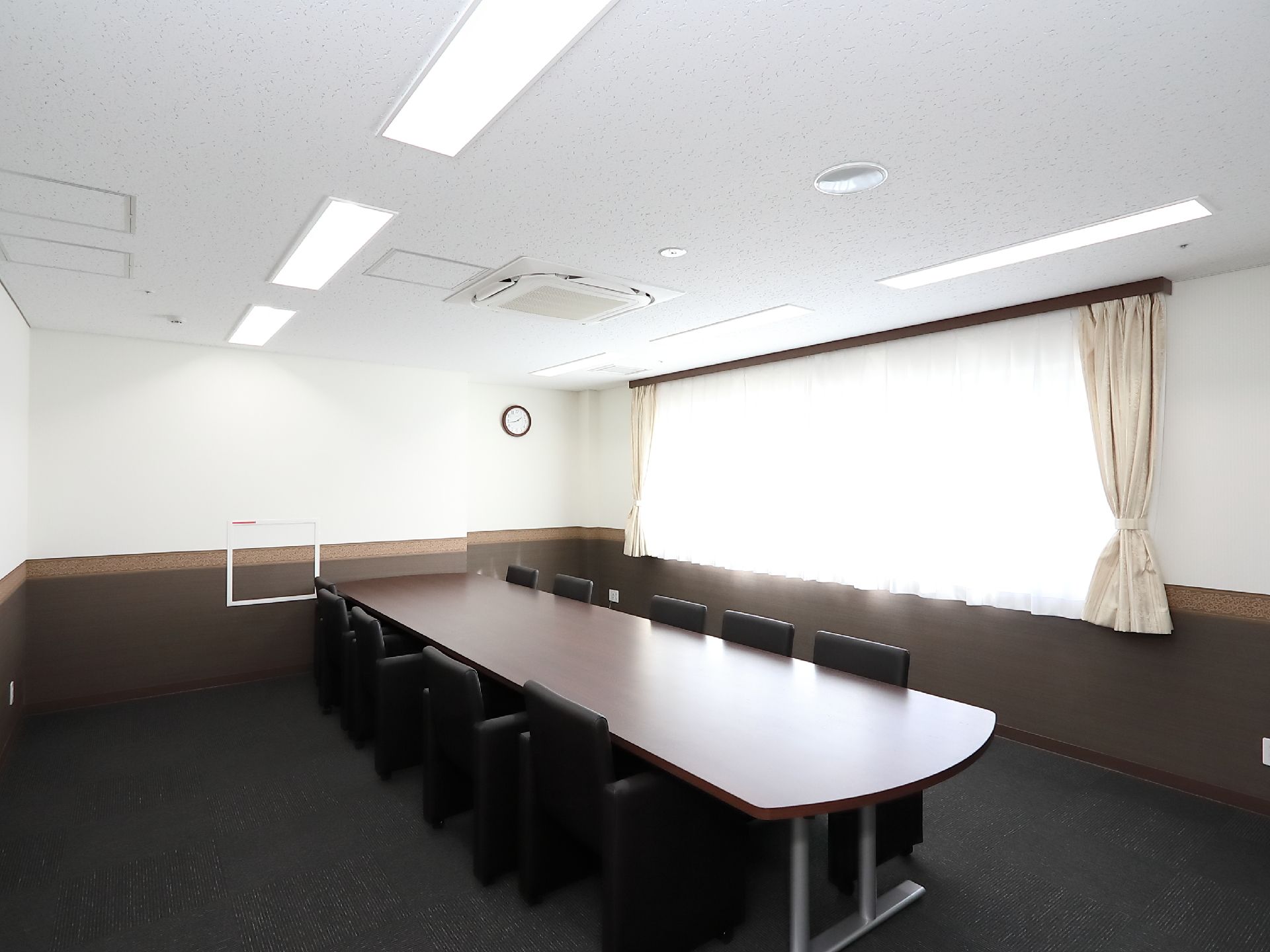 広いスペースに向かい合った席のある相談室がある。重厚感あるデスクとチェアが置かれている。窓から光が入り明るい。