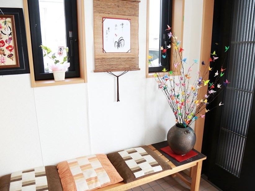 木製の横長ベンチには、小さな座布団が置かれ、花瓶には折り紙の鶴で作られた花が飾られている。墨絵の掛け軸があり、和風の飾りつけである。