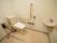 淡い水玉模様の壁紙が施された、柔らかい印象を与えるトイレスペース。便器前方の角に手洗器が設置されており、ハンドソープが用意されている。