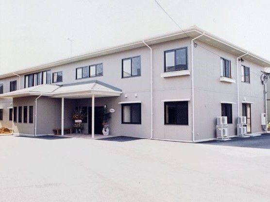 白っぽい外壁、左側にひさしの付いた玄関ポーチのある2階建ての建物