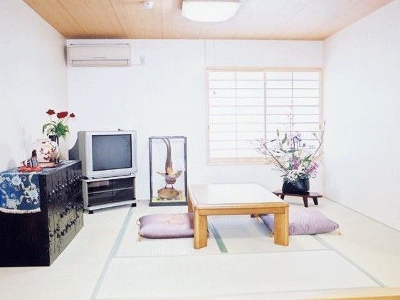 白っぽい壁の畳敷き、左の壁面に黒いタンスとテレビがあり、右奥に障子のはまった窓がある和室