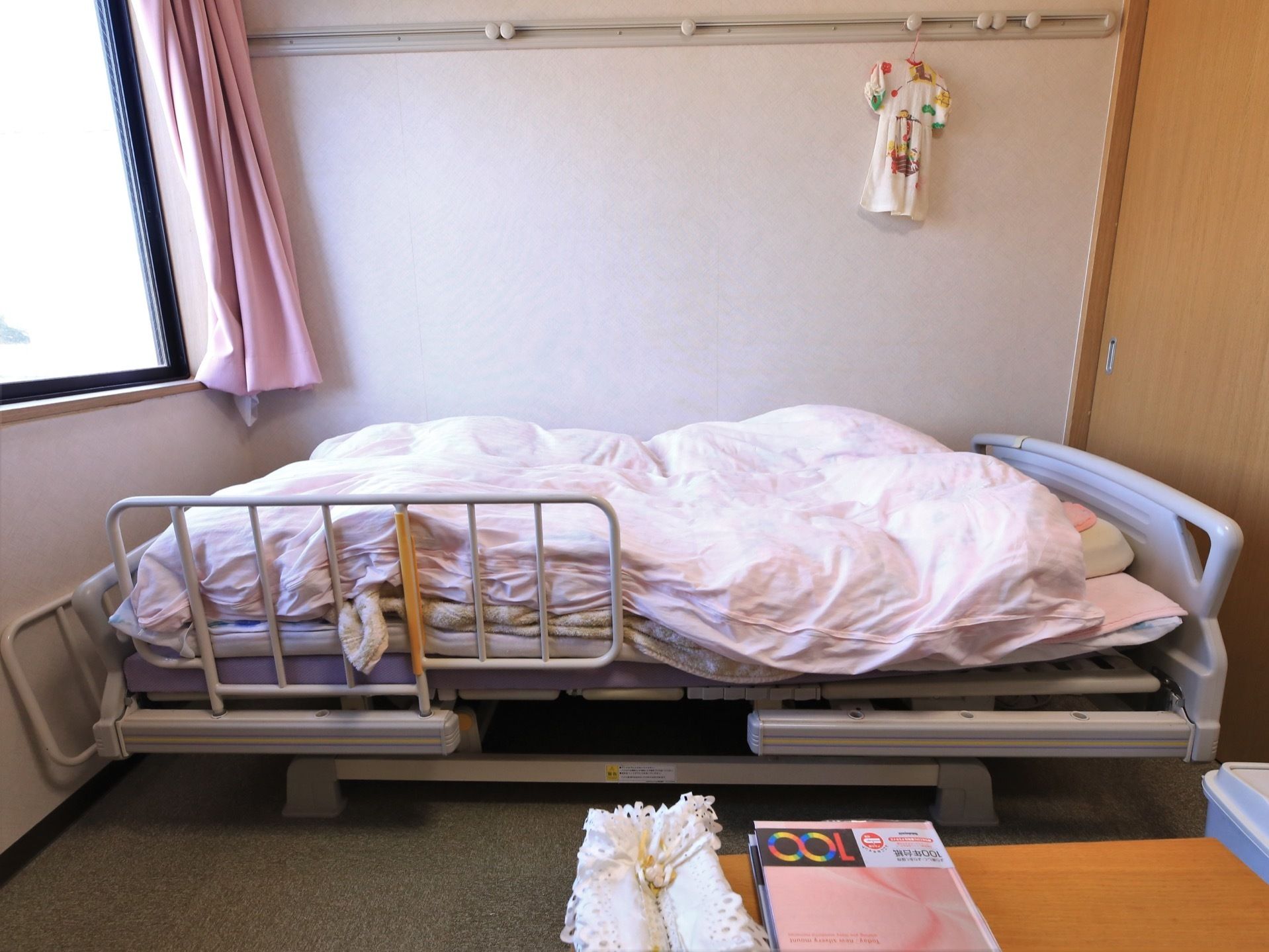 壁際に介護用ベッドが置かれ、ピンクの布団が敷かれている。壁の上部にハンガーなどが掛けられるレールが取りつけられている。