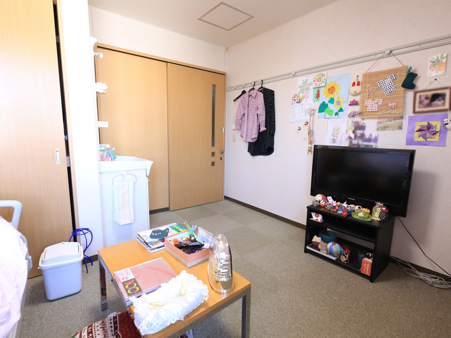 居室入口は木製扉の引き戸になっている。入口横に洗面台があり、タオルが掛けられている。壁際に液晶テレビがある。