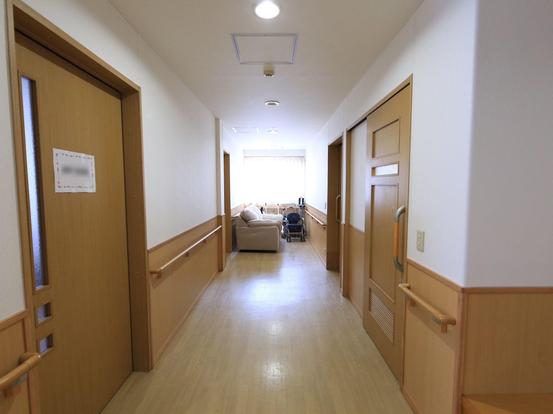 廊下の床はフローリングになっており、板材と漆喰の白い壁が続いている。両側に木製の引き戸が並んでいる。