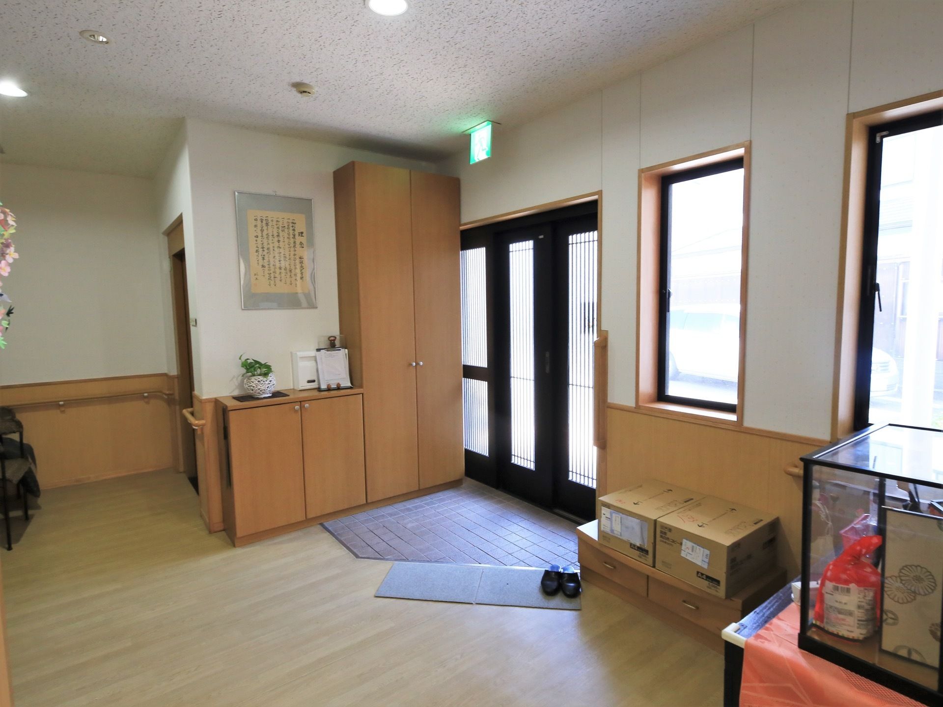 黒い扉の玄関が閉められている。扉の前には天井まで届くサイズの収納と、腰ほどの高さの棚がある。スリッパが１足置かれている。