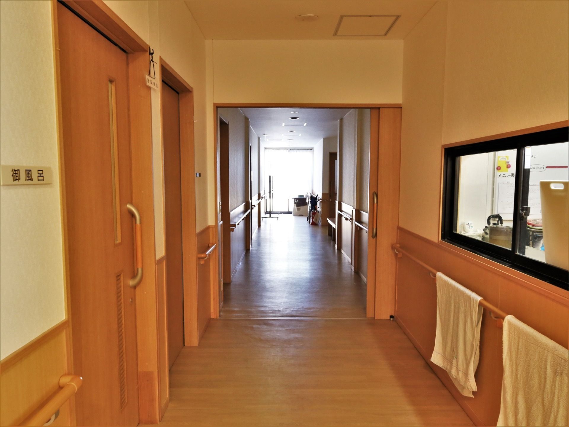 左手に引き戸の扉が並び、一番手前に浴室へ続く扉がある。右側には小窓があり、キッチンの中が見えている。