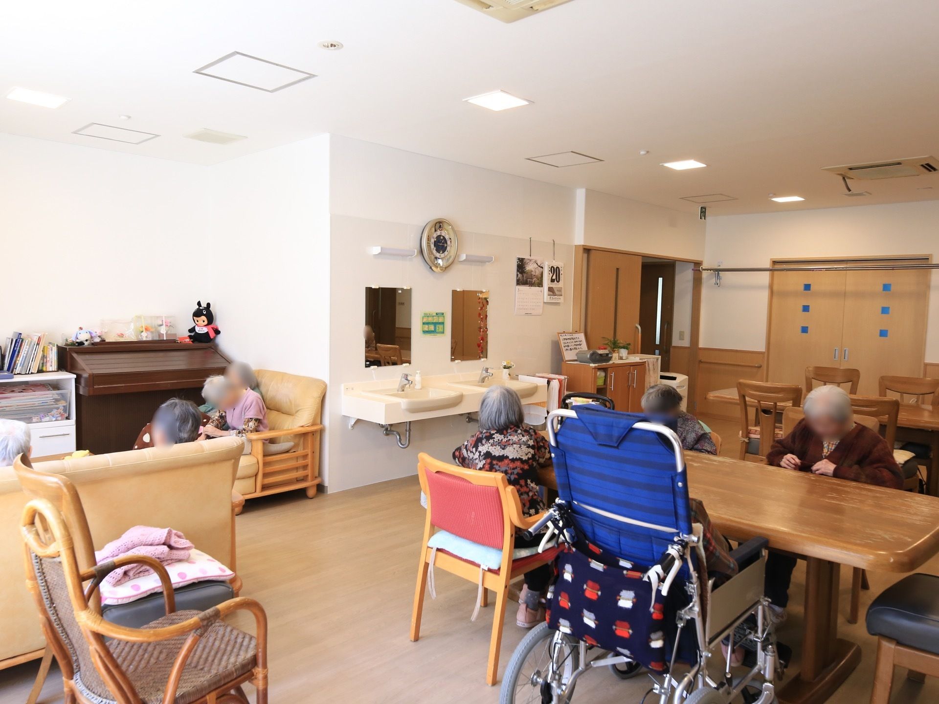 左手奥にベージュのソファセットが並び、入居者様がくつろいでいる。奥に洗面台が２か所に設置されている。
