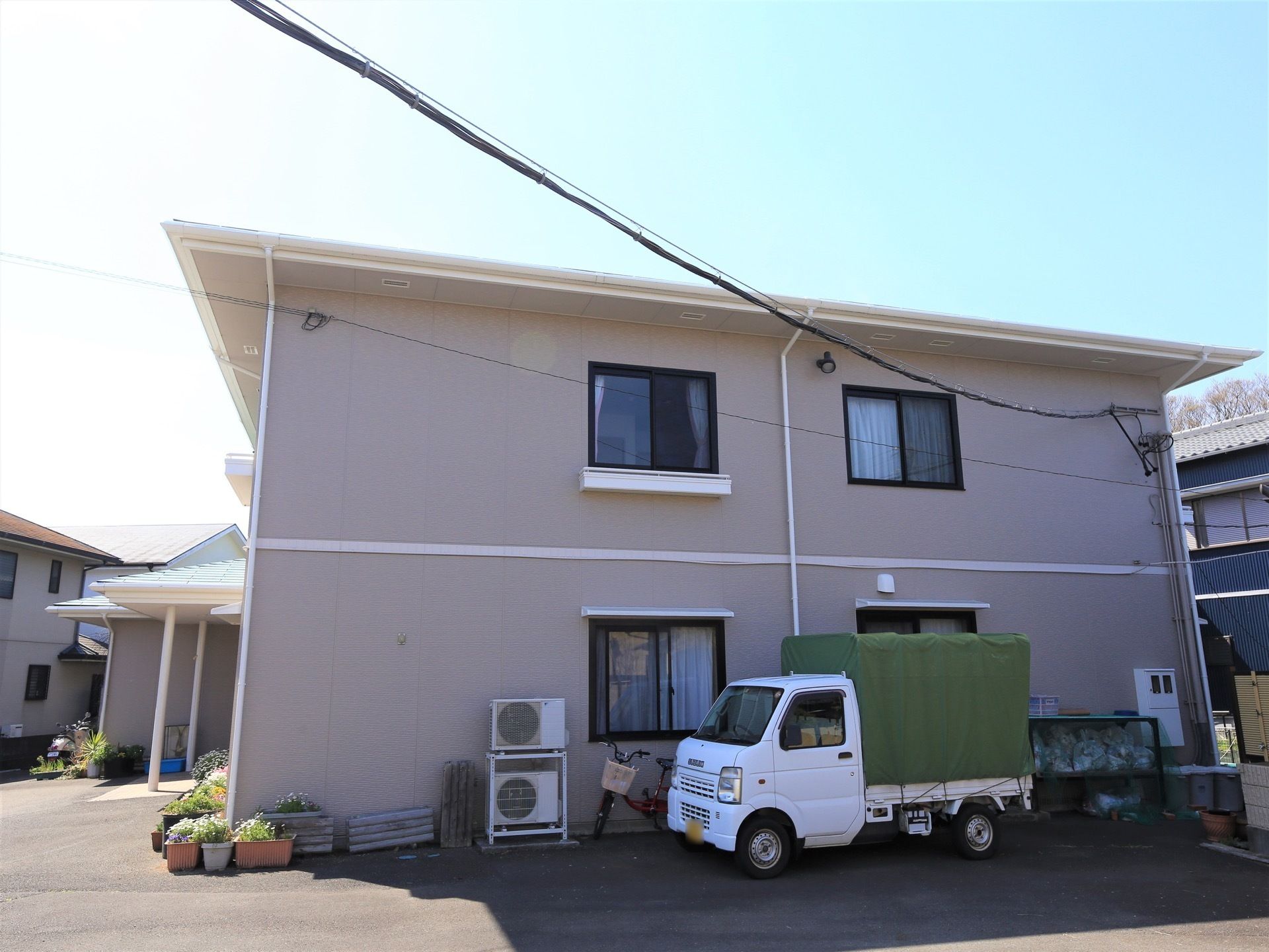 ベージュの外壁の建物で２階建てである。一般のアパートのような雰囲気が漂っている。軽トラックが停められている。