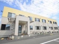 玄関上には屋根とひさしがある。玄関までは左右に分かれて、手すり付きの階段とスロープが設けられている。手前には駐車スペースがある。