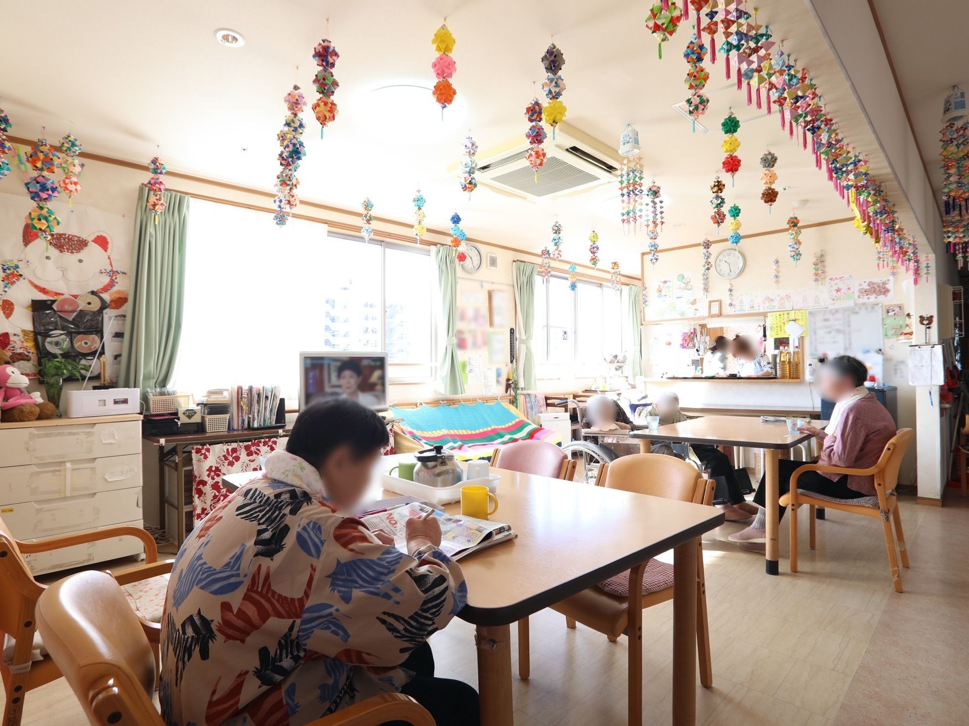 入居者様の折り紙作品がたくさん天井から吊るされた、家庭的な雰囲気の共有スペース。厨房にいるスタッフと、コンタクトを交わすことができる。