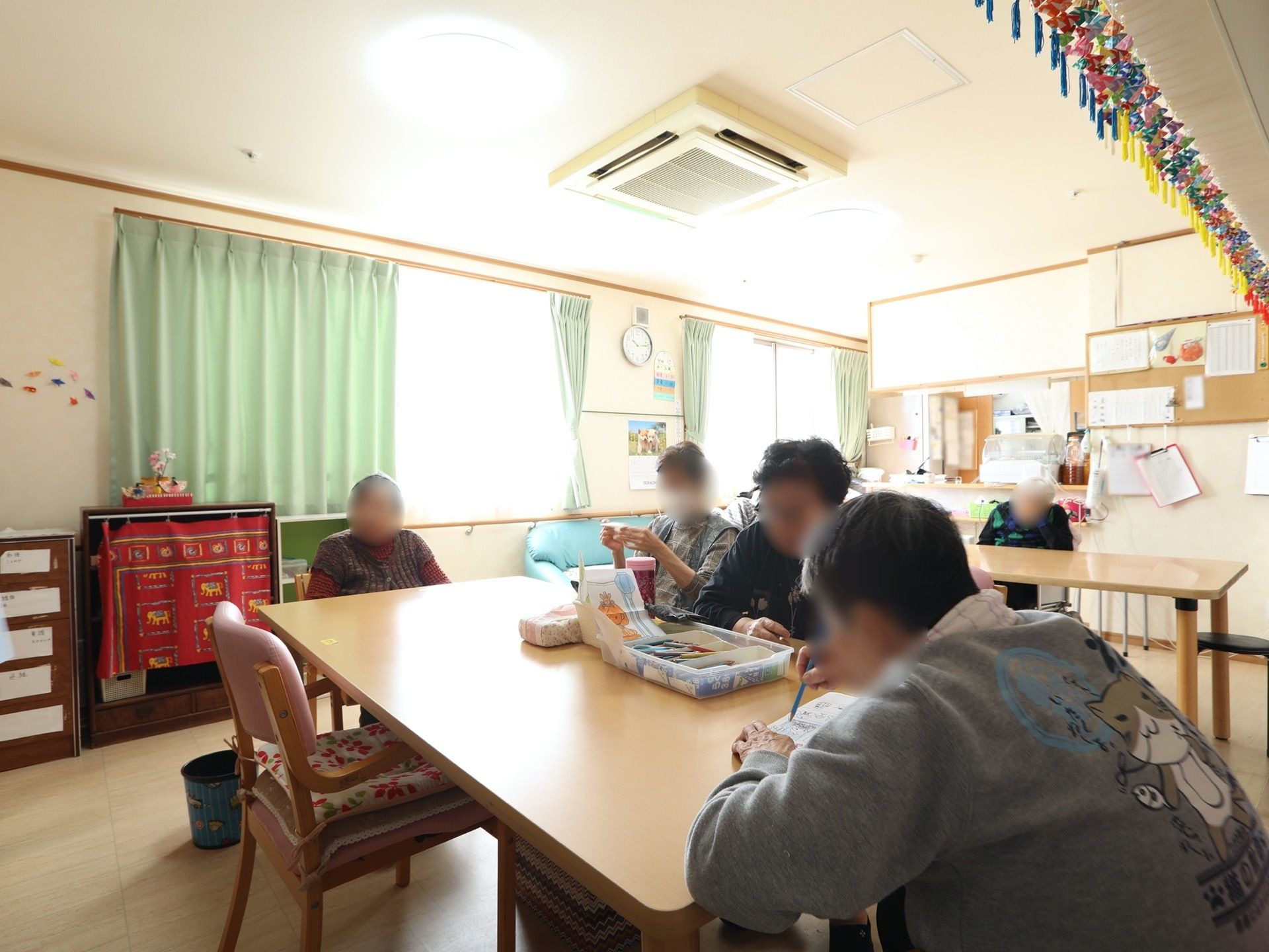 日中共有スペースでくつろいでいる入居者様のご様子。お食事や工作などの手作業が余裕をもって行えるよう、大きいテーブルが用意されている。
