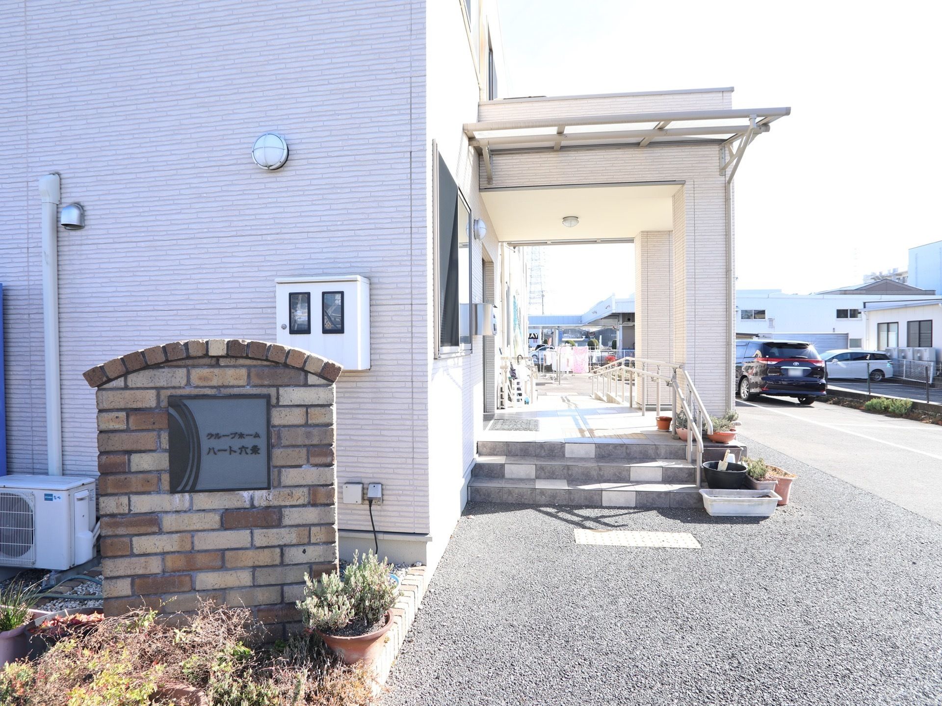 玄関前では、アーチ型の施設の銘板が来訪者様をお迎えしている。入り口前は広いスペースが確保されている。