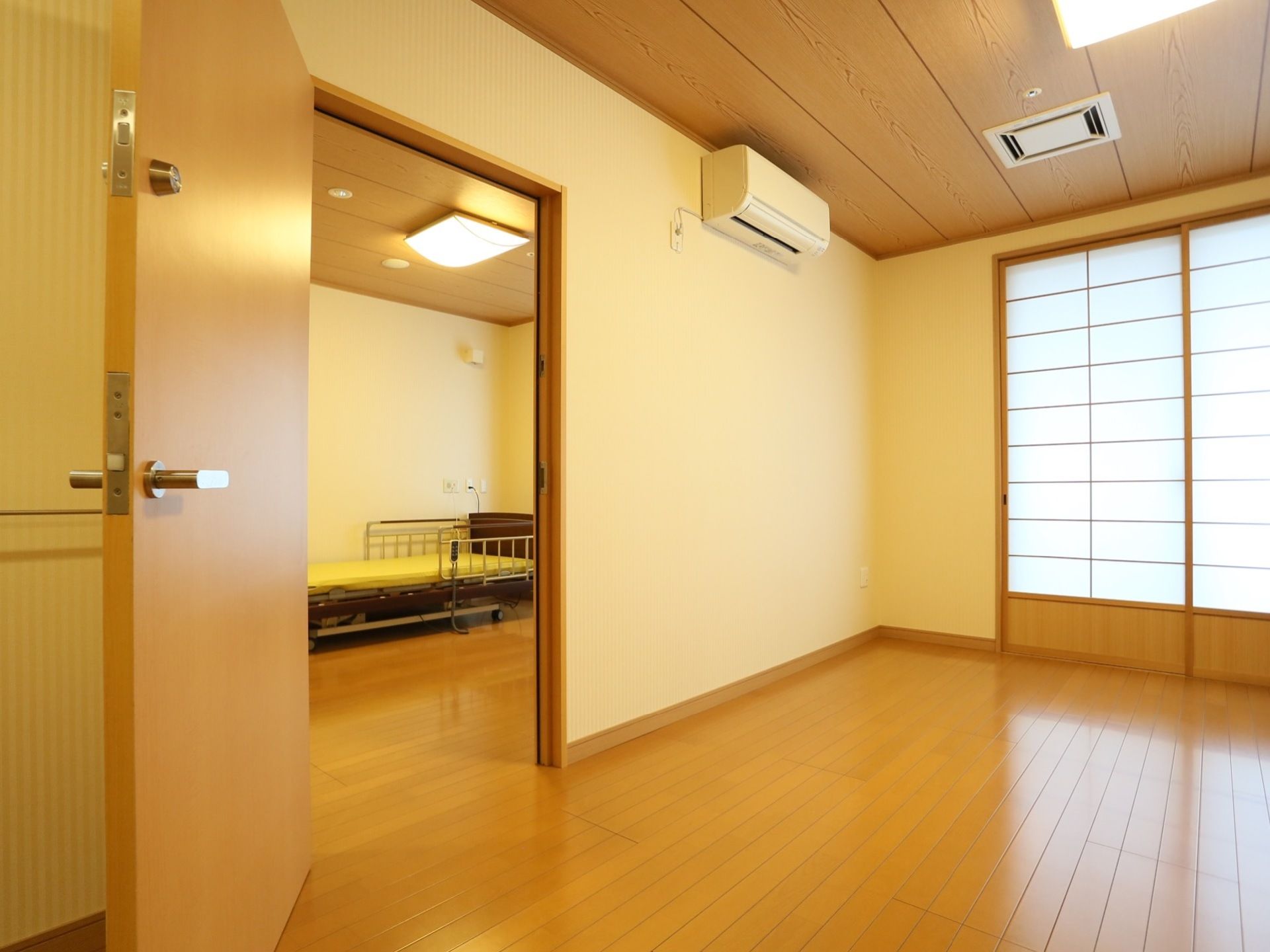 ２間続きのフローリング床面の居室になっている。介護ベッドのほか、エアコンも設置されている。天井は木目調である。