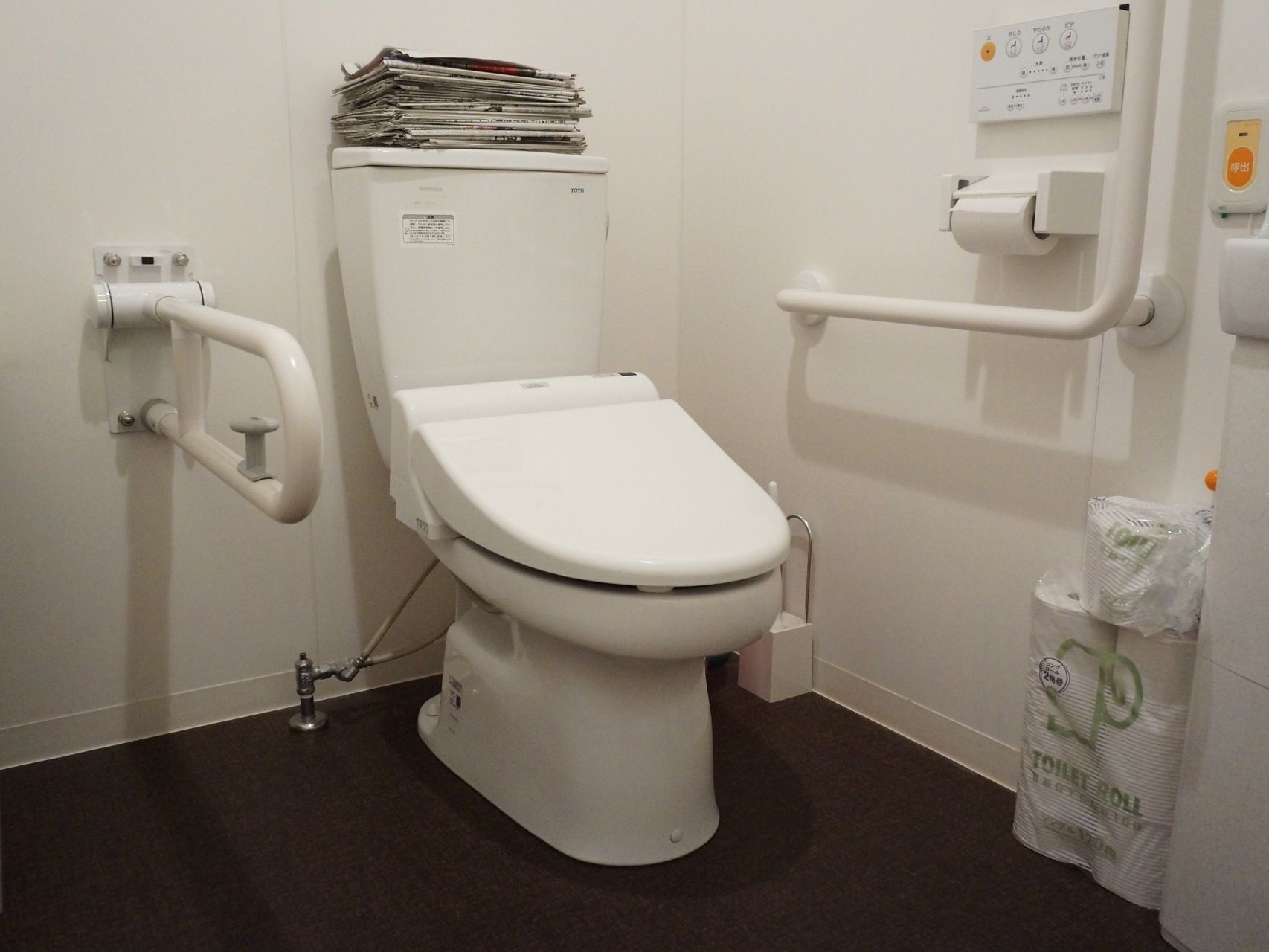 便器が正面にある。右壁にはＬ字型の手すりとトイレットペーパーが付いている。右手前には緊急呼び出し装置がある。