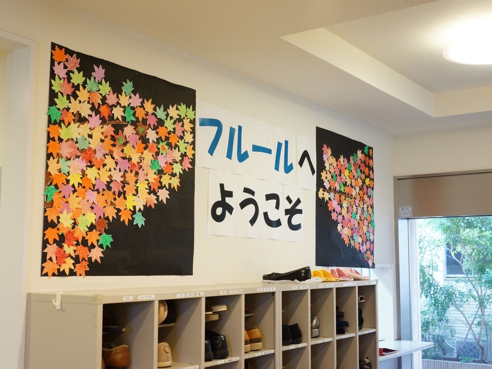 上側には出迎える際の文言が書かれており、その左右両側には紅葉を模した飾りが沢山付いている。下側には靴箱がある。