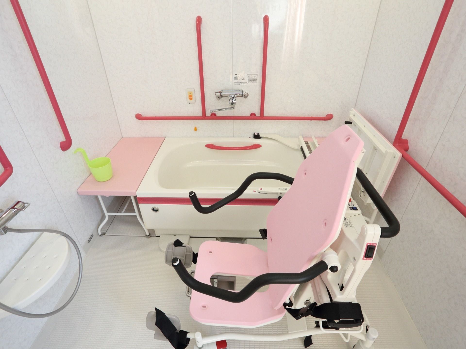 座浴用の器具がある。壁には鮮やかな色の手すりが複数取り付けられている。緊急用の呼出ボタンが設置されている。