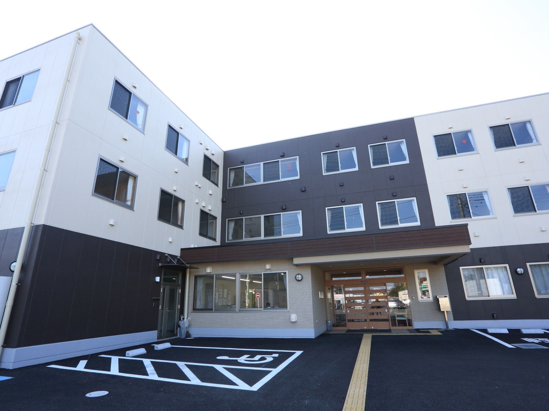 ３階建て。玄関に向かって点字ブロックが設置されている。建物の前には駐車場があり、車椅子専用のスペースもある。
