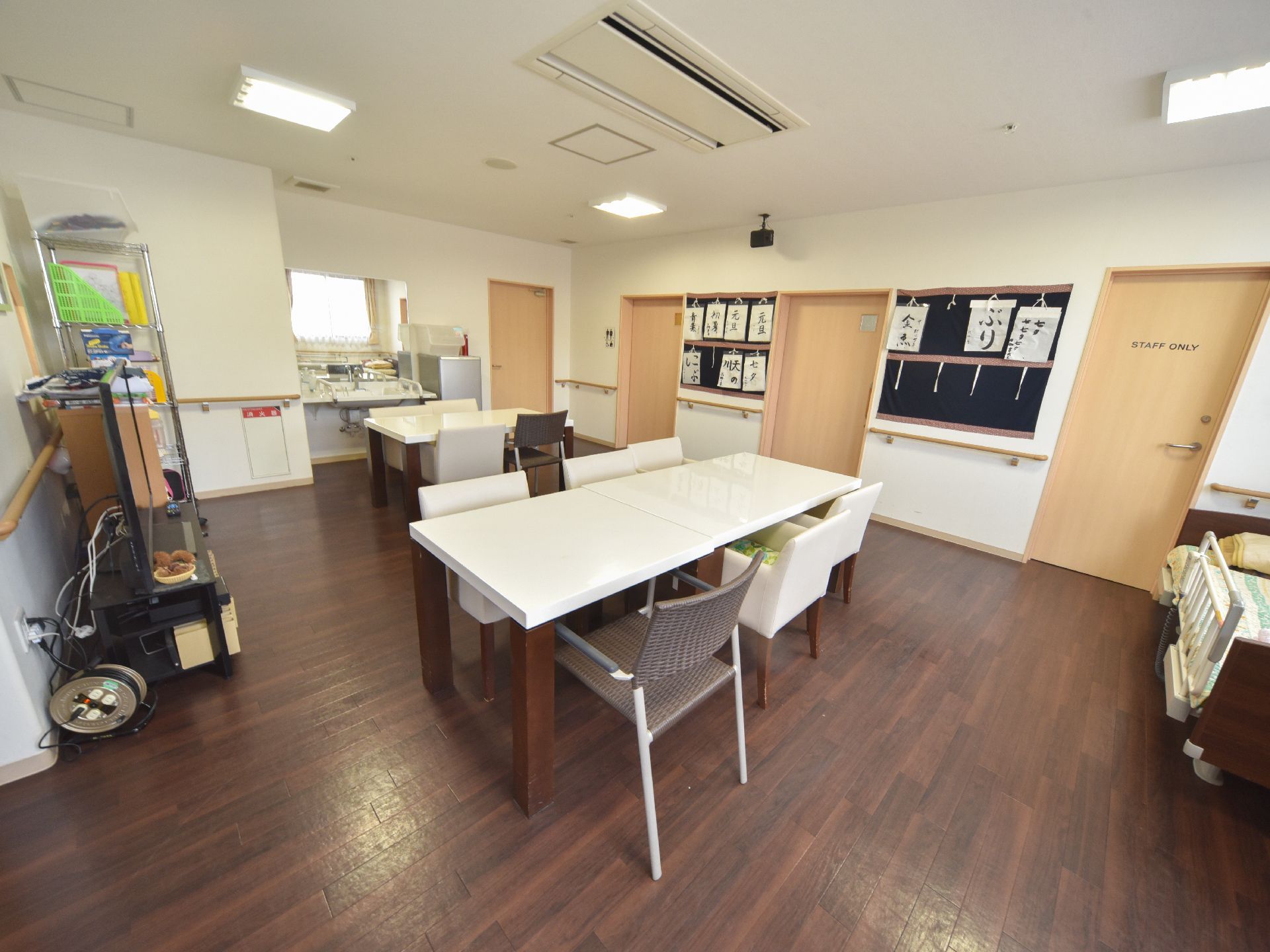 右側の壁には書道の作品を飾るスペースがある。天井にはエアコンが付いている。右側から中央奥にかけて複数の扉がある。