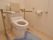正面には洋式の便器がある。背もたれとひじ掛けが付いている。右壁にはトイレットペーパーがあり、その近くには緊急呼び出し装置がある。