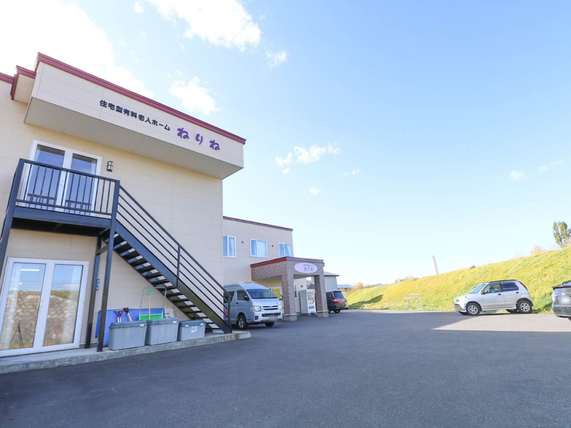 豊かな自然に恵まれた環境で、周囲には高い建物がなく見晴らしが良い。敷地内には、複数台の車が停められている。