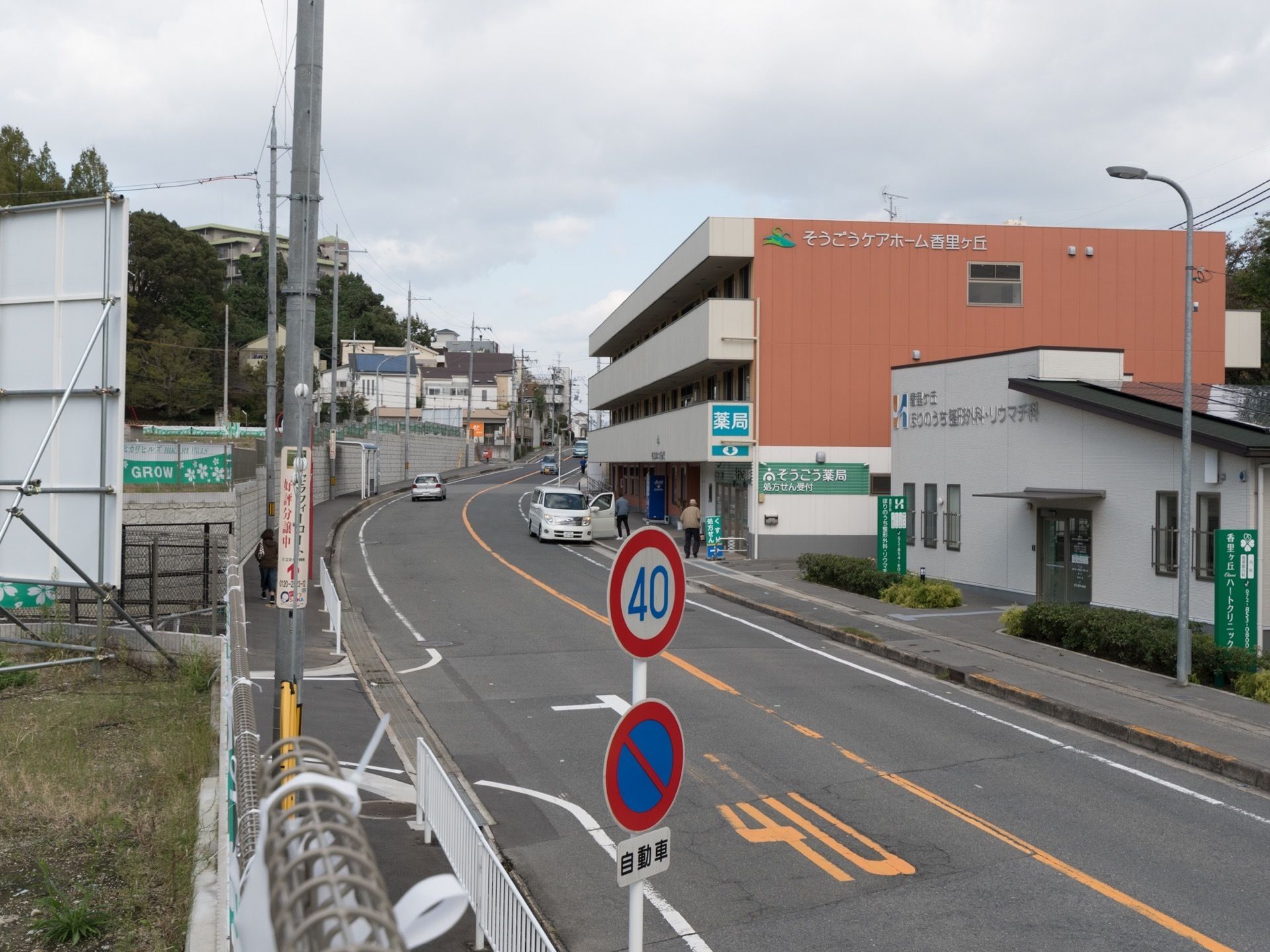 施設は道路に面して建てられている。施設の前には乗用車が止められていて、扉が開けられている。近くには男性が立っている。